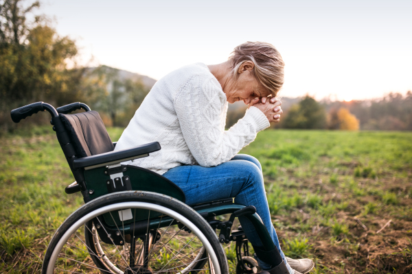 A senior woman in wheelchair in nature. A woman praying.