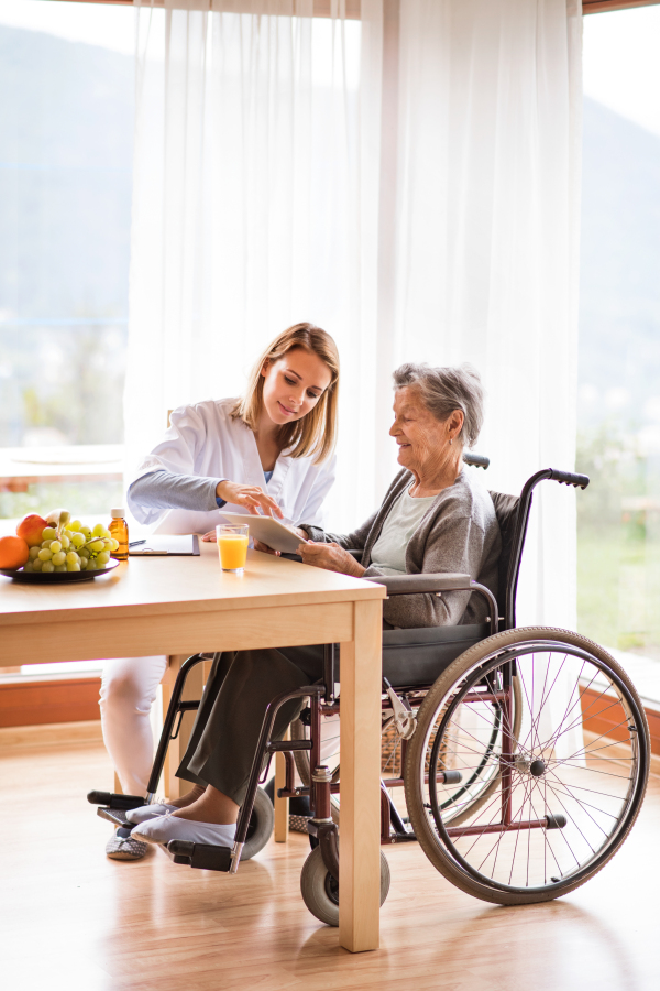 Health visitor and a senior woman with tablet during home visit. A nurse talking to an elderly woman.