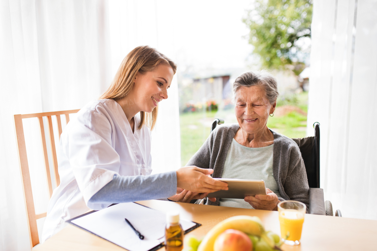 Health visitor and a senior woman with tablet during home visit. A nurse talking to an elderly woman.