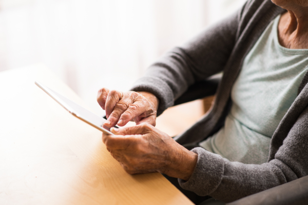 Unrecognizable senior woman in a wheelchair with tablet at home. An elderly woman sitting at the table.