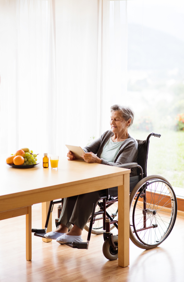 Senior woman in a wheelchair with tablet at home. An elderly woman sitting at the table.