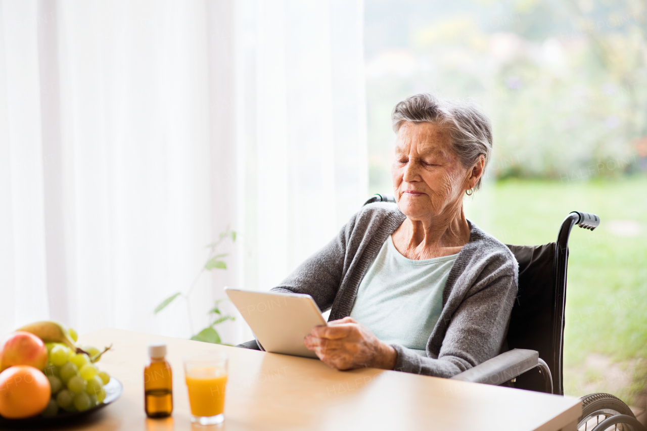 Senior woman in a wheelchair with tablet at home. An elderly woman sitting at the table.