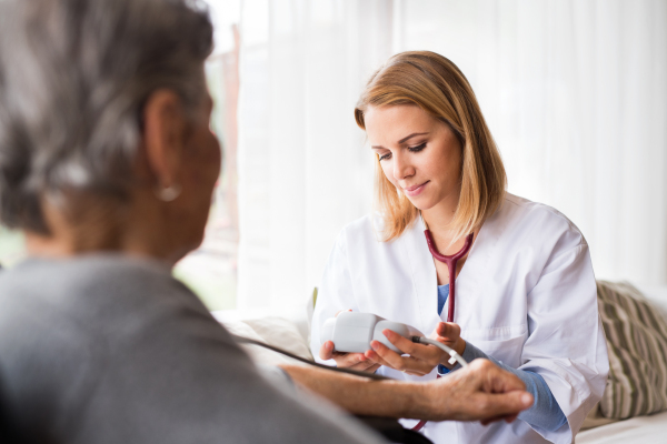 Health visitor and a senior woman during home visit. A nurse checking blood pressure of a woman.