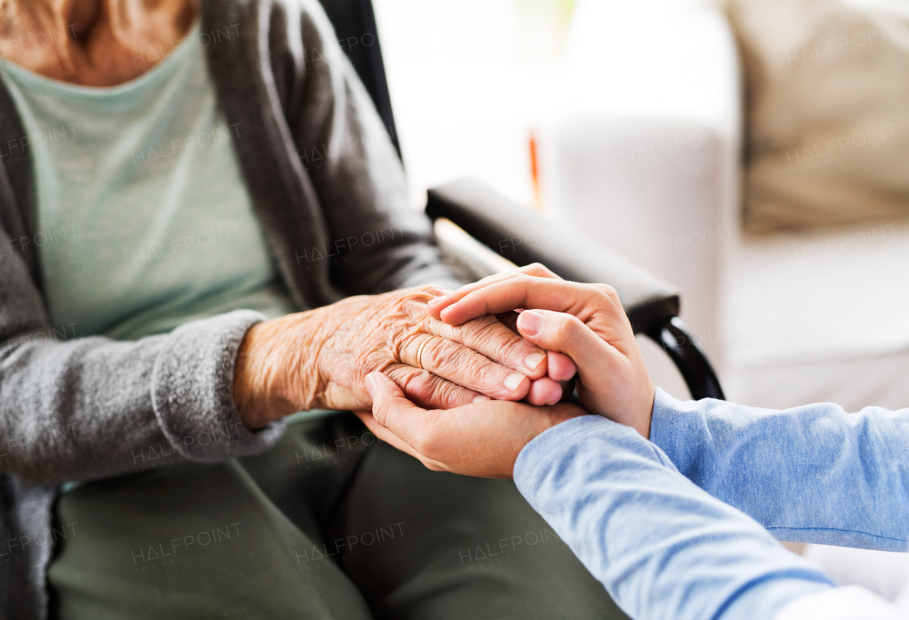 Unrecognizable health visitor and a senior woman during home visit. Nurse holding both hands of an eldelry woman. Close up.