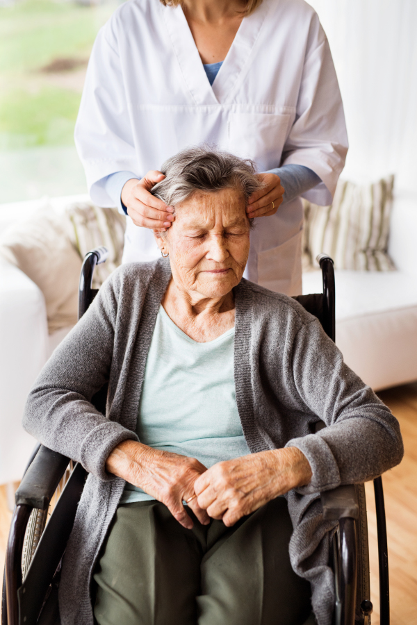 Health visitor and a senior woman during home visit. Unrecognizable nurse giving woman temple massage.