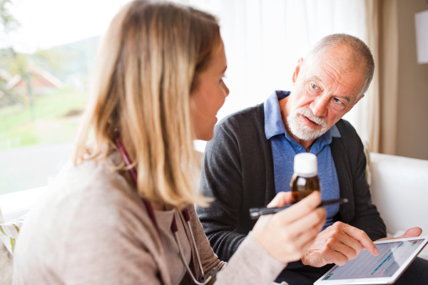 Health visitor and a senior man during home visit. A female nurse or a doctor showing test results on a tablet.