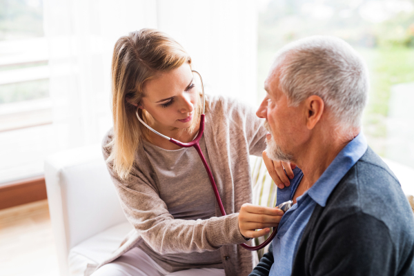 Health visitor and a senior man during home visit. A female nurse or a doctor examining a man.