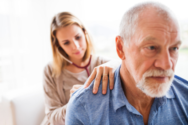 Health visitor and a senior man during home visit. A female nurse or a doctor examining a man.