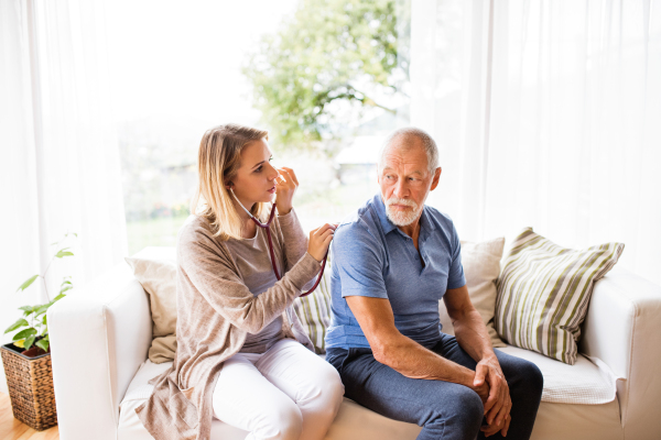 Health visitor and a senior man during home visit. A female nurse or a doctor examining a man.