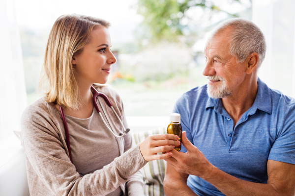 Health visitor and a senior man during home visit. A female nurse or a doctor giving medicine to a man. Close up.