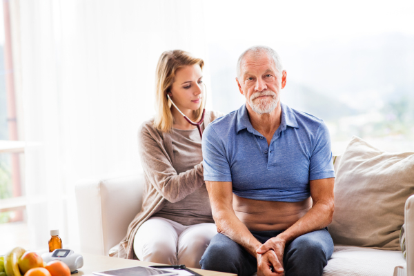 Health visitor and a senior man during home visit. A female nurse or a doctor examining a man.