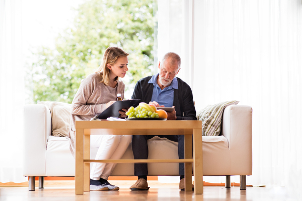 Health visitor and a senior man during home visit. A female nurse or a doctor showing test results on a tablet.