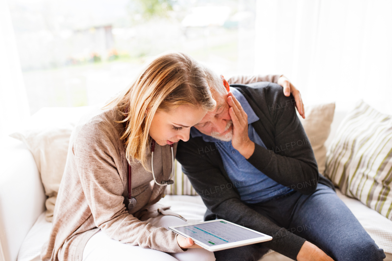 Health visitor and a senior man during home visit. A female nurse or a doctor showing test results on a tablet.