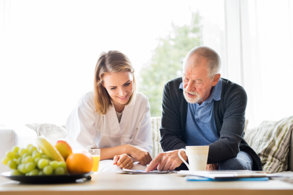 Health visitor and a senior man during home visit. A female nurse or a doctor showing test results on a tablet.