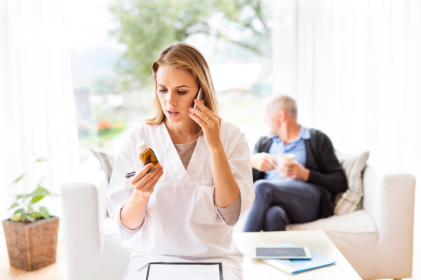 Health visitor with smartphone and a senior man during home visit. A female nurse or a doctor making a phone call.