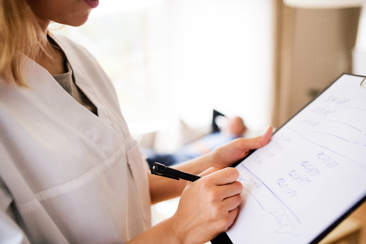 Unrecognizable health visitor and a senior man during home visit. A female nurse or a doctor making notes. Close up.