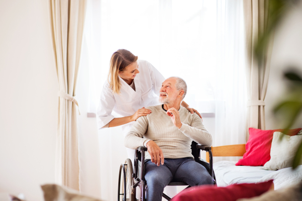 Health visitor and a senior man in a wheelchair during home visit. A nurse or a physiotherapist talking to a man.