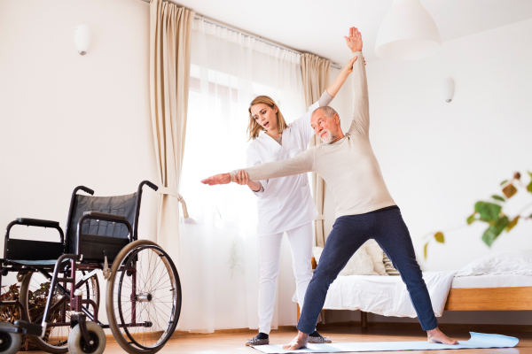 Health visitor and a senior man during home visit. A nurse or a physiotherapist helping a senior man exercise.