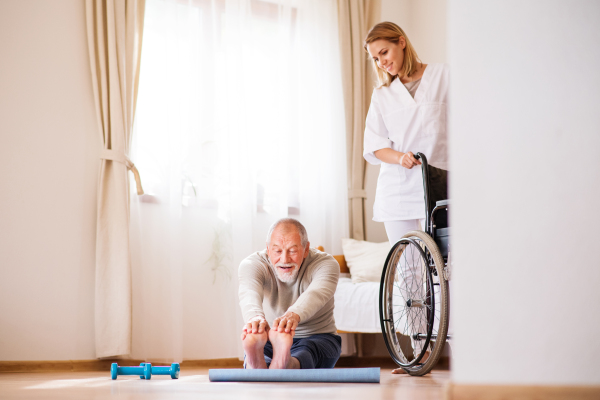 Health visitor and a senior man during home visit. A nurse or a physiotherapist helping a senior man exercise.