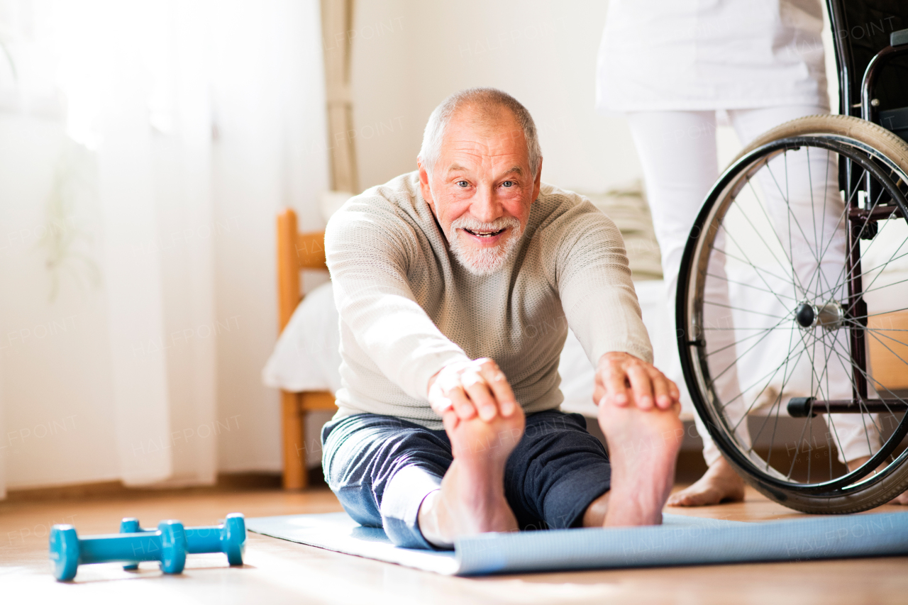 Unrecognizable health visitor and a senior man during home visit. Senior man doing exercise.