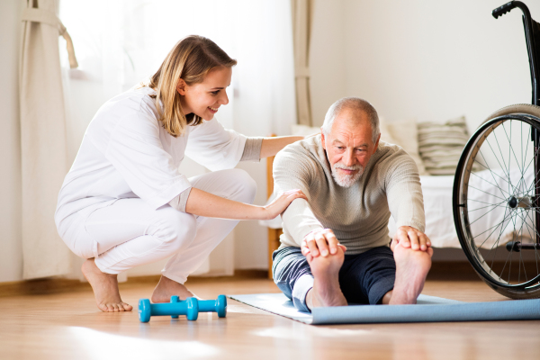 Health visitor and a senior man during home visit. A nurse or a physiotherapist helping a senior man exercise.