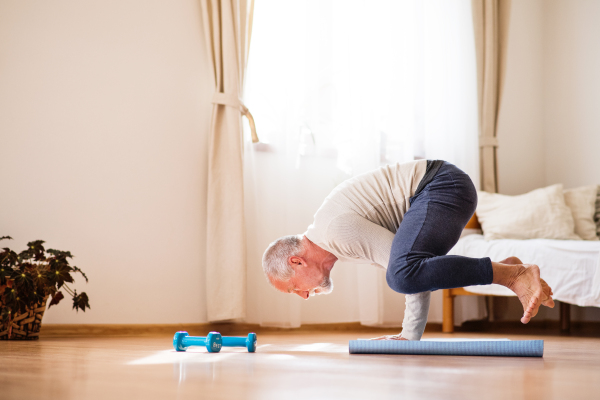 Active senior man doing exercise at home. Man next to a wheelchair doing frogstand. Knees on elbows.