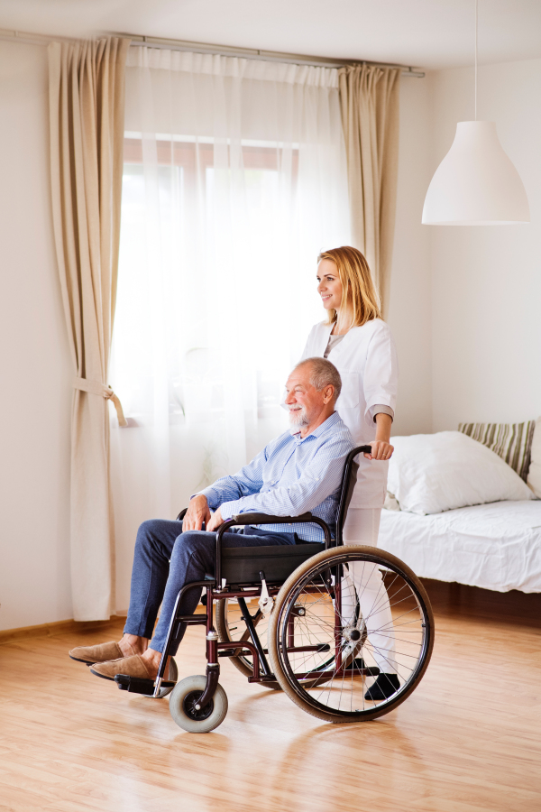 Health visitor or a nurse and a senior man in a wheelchair during home visit.