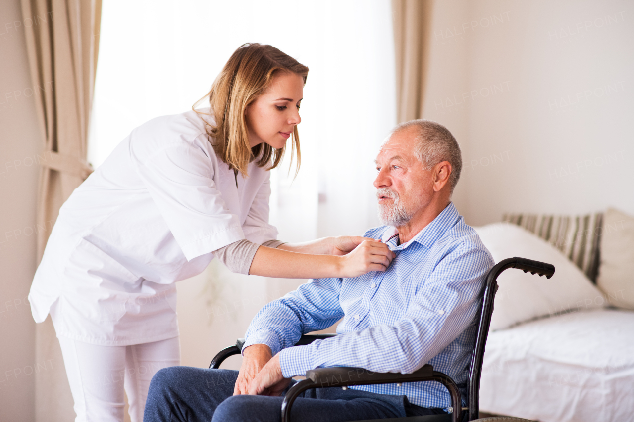 Health visitor or a nurse and a senior man in a wheelchair during home visit.