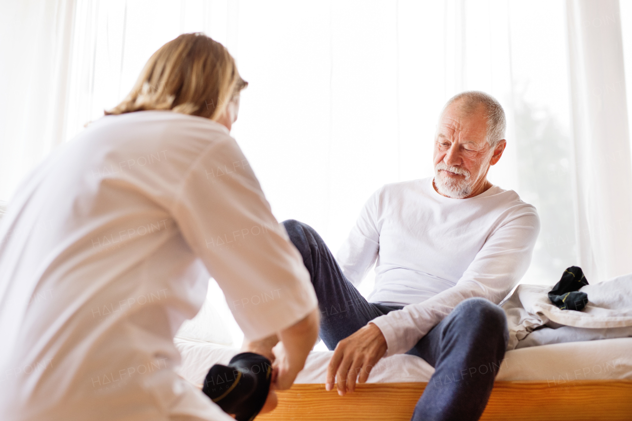 Health visitor and a senior man during home visit. A nurse helping a senior man to put socks on.