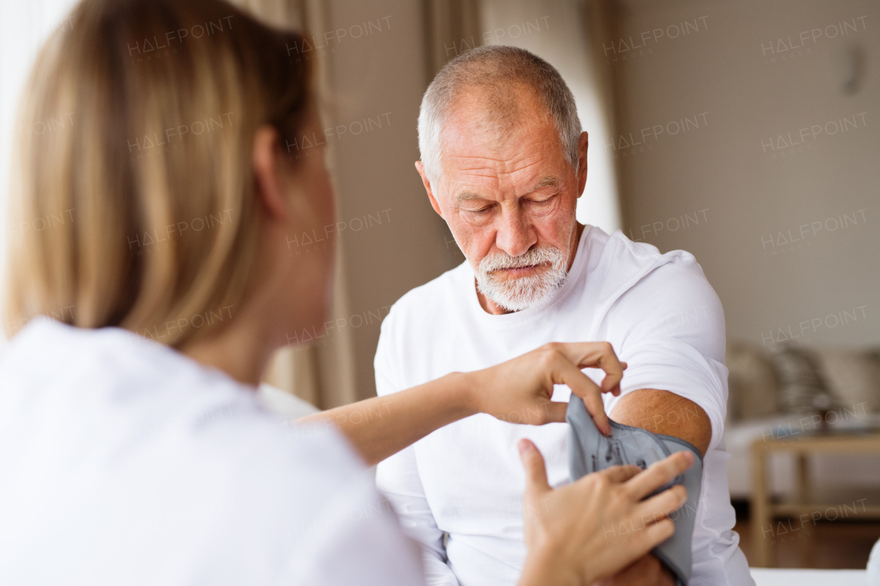 Health visitor and a senior man during home visit. A nurse checking blood pressure of a man.