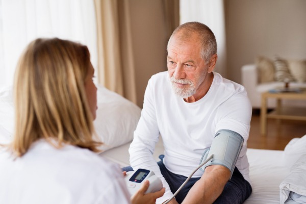 Health visitor and a senior man during home visit. A nurse checking blood pressure of a man.