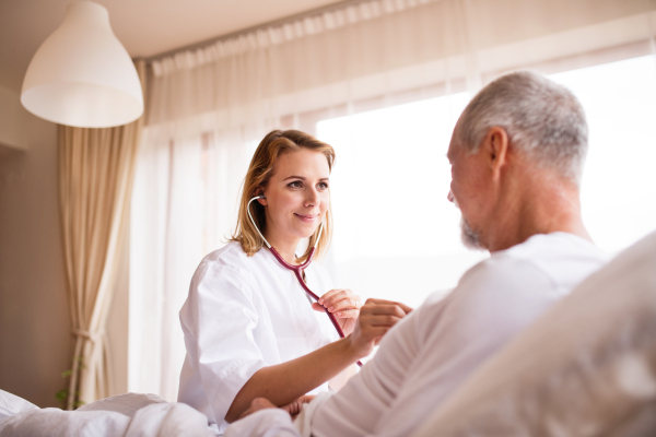 Health visitor and a senior man during home visit. A female nurse or a doctor examining a man.