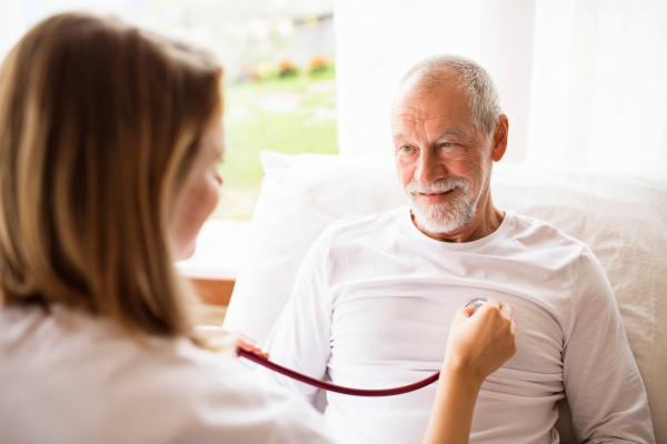 Health visitor and a senior man during home visit. A female nurse or a doctor examining a man.