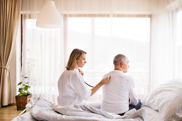 Health visitor and a senior man during home visit. A female nurse or a doctor examining a man.