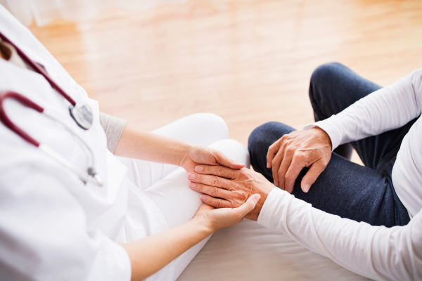 Unrecognizable health visitor and a senior man during home visit. A nurse holding a hand of a man.