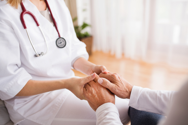 Unrecognizable health visitor and a senior man during home visit. A nurse holding hands of a man.