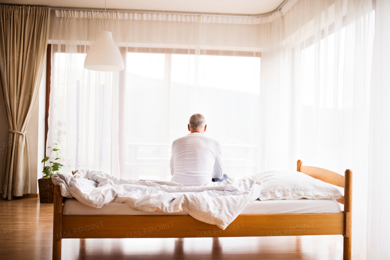 Senior man sitting on bed at home. Rear view.