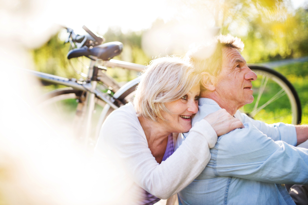 Beautiful senior couple with bicycles outside in spring nature under blossoming trees.