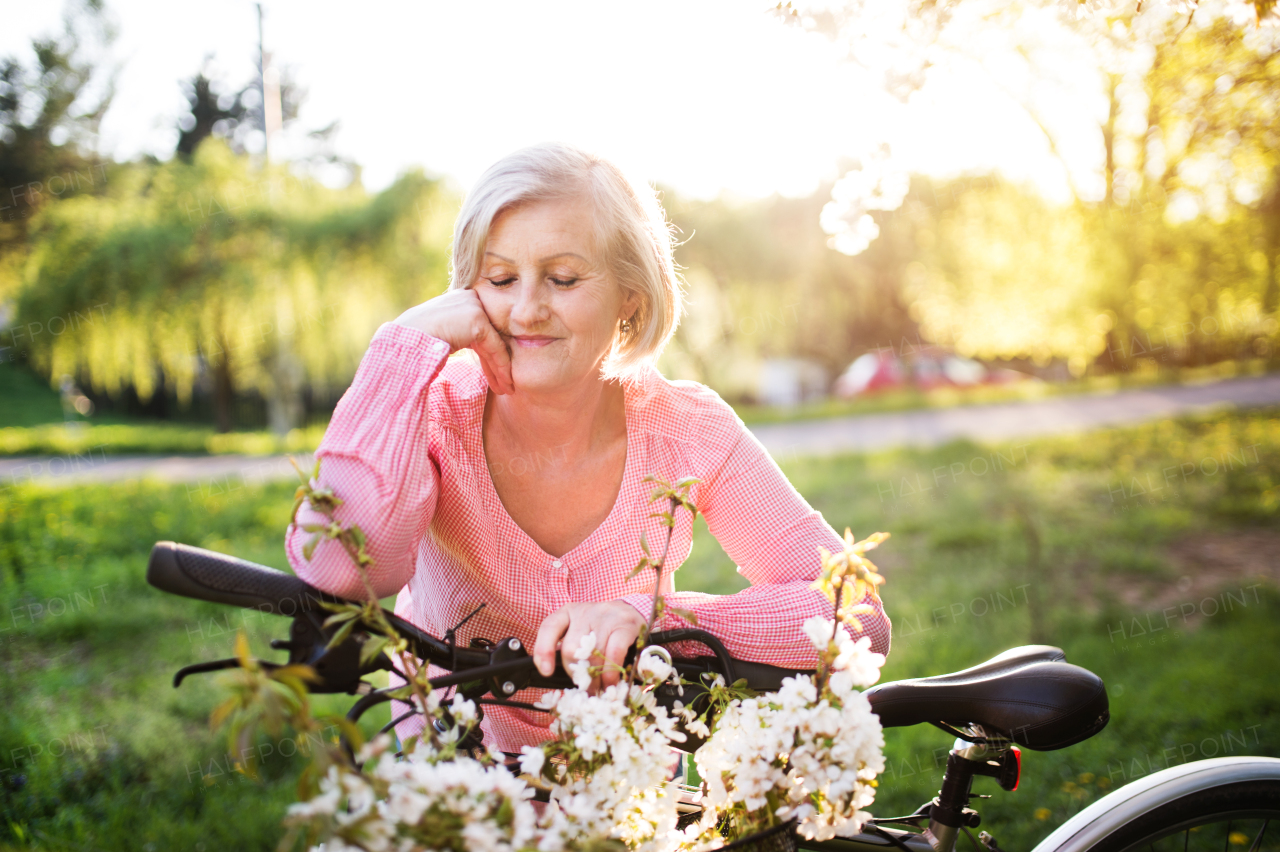 Beautiful senior woman with bicycle standing outside in spring nature.