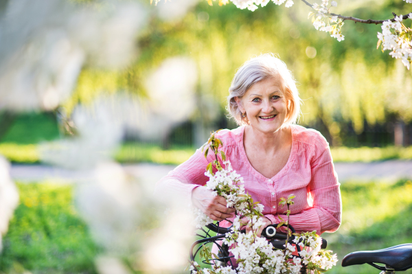 Beautiful senior woman with bicycle standing outside in spring nature.