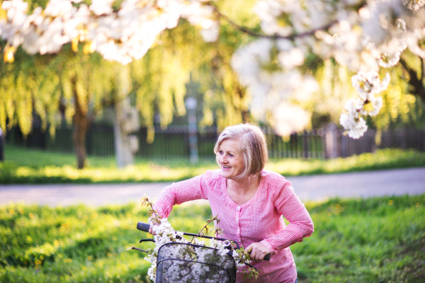 Beautiful senior woman with bicycle outside in spring nature, resting.