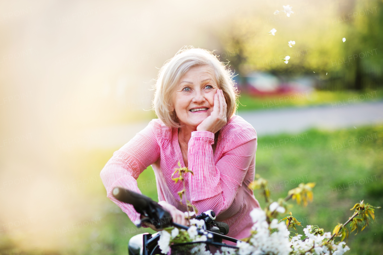 Beautiful senior woman with bicycle outside in spring nature, resting.