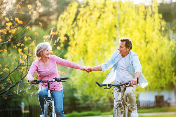 Beautiful senior couple with bicycles outside in spring nature cycling and holding hands.