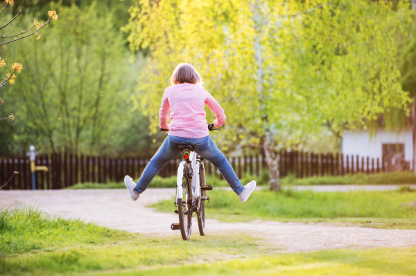 Senior woman with bicycle cycling outside in spring nature, having fun. Rear view.