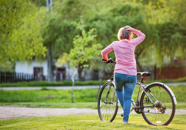 Senior woman with bicycle outside in spring nature, resting. Rear view. Copy space.