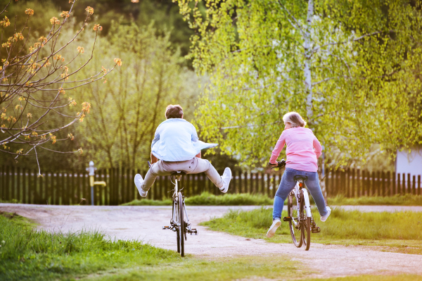 Beautiful senior couple with bicycles cycling outside in spring nature, having fun. Rear view.