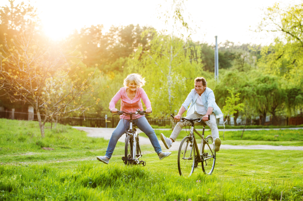 Beautiful senior couple with bicycles cycling outside in spring nature, having fun.