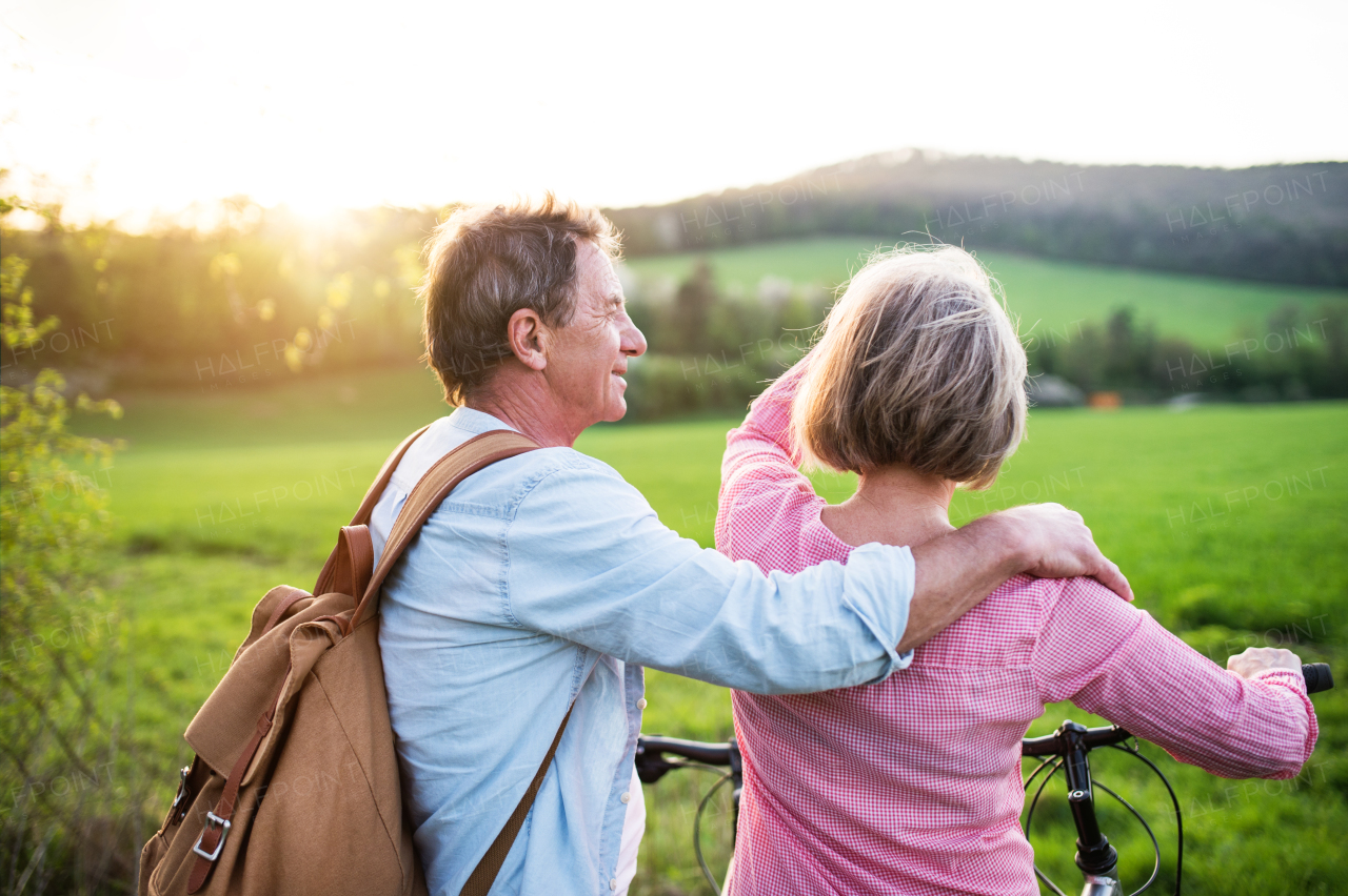 Beautiful senior couple with bicycles outside in spring nature. A man and woman in love. Rear view.