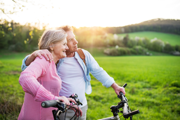 Beautiful senior couple outside in spring nature, standing with bicycles on grassland.