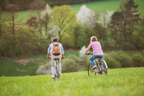 Beautiful senior couple outside in spring nature, with bicycles cycling on grassland. Rear view.